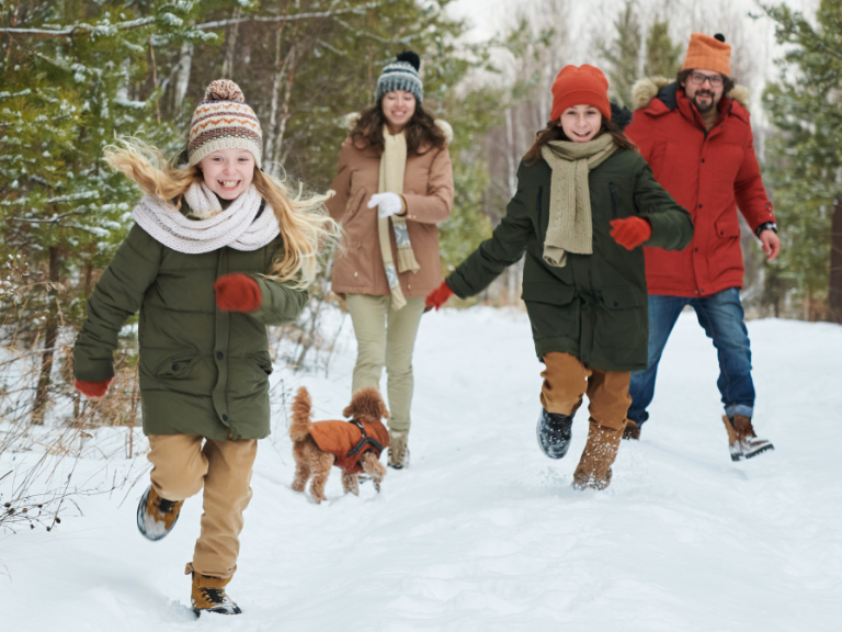 Familie mit zwei Mädchen und Hund laufen durch den chnee