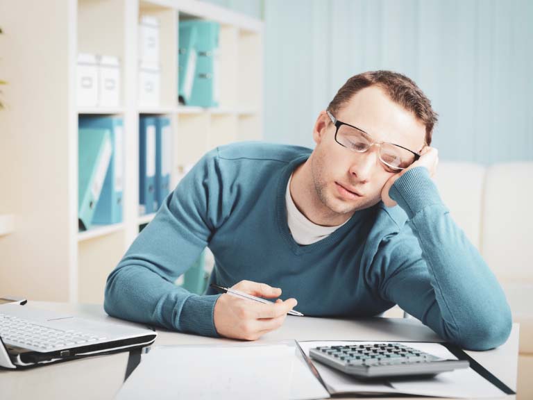 Junger Mann, der bei der Arbeit vor seinem Laptop eingenickt ist